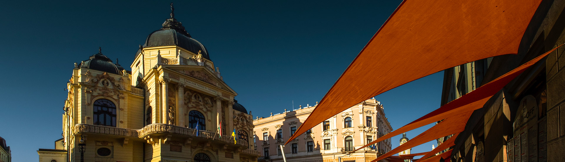 A Pécsi Nemzeti Színház külső képe nappali fényben rozsdabarna színű napvitrolákkal az előtérben