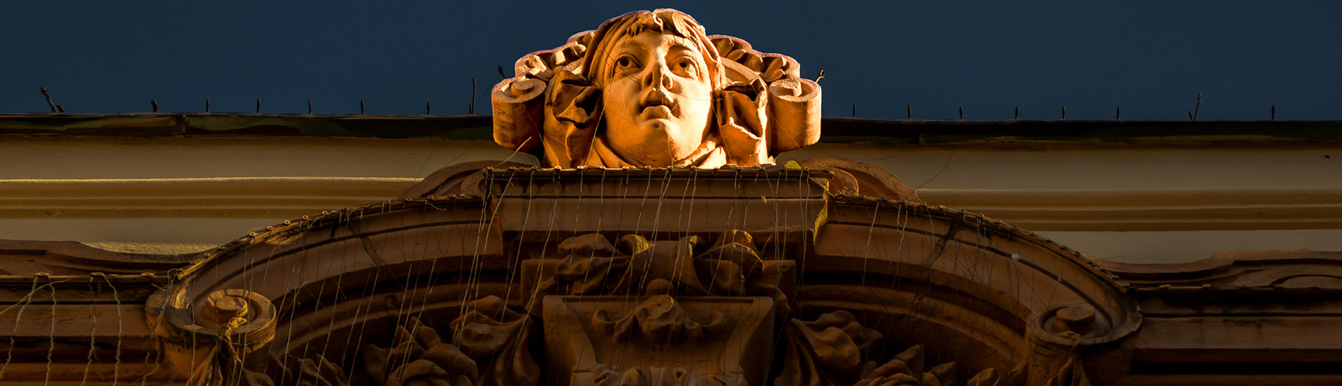A Pécsi Nemzeti Színház külső homlokazti oldalán surulófényben látható egy szecessziós fej premierplánban